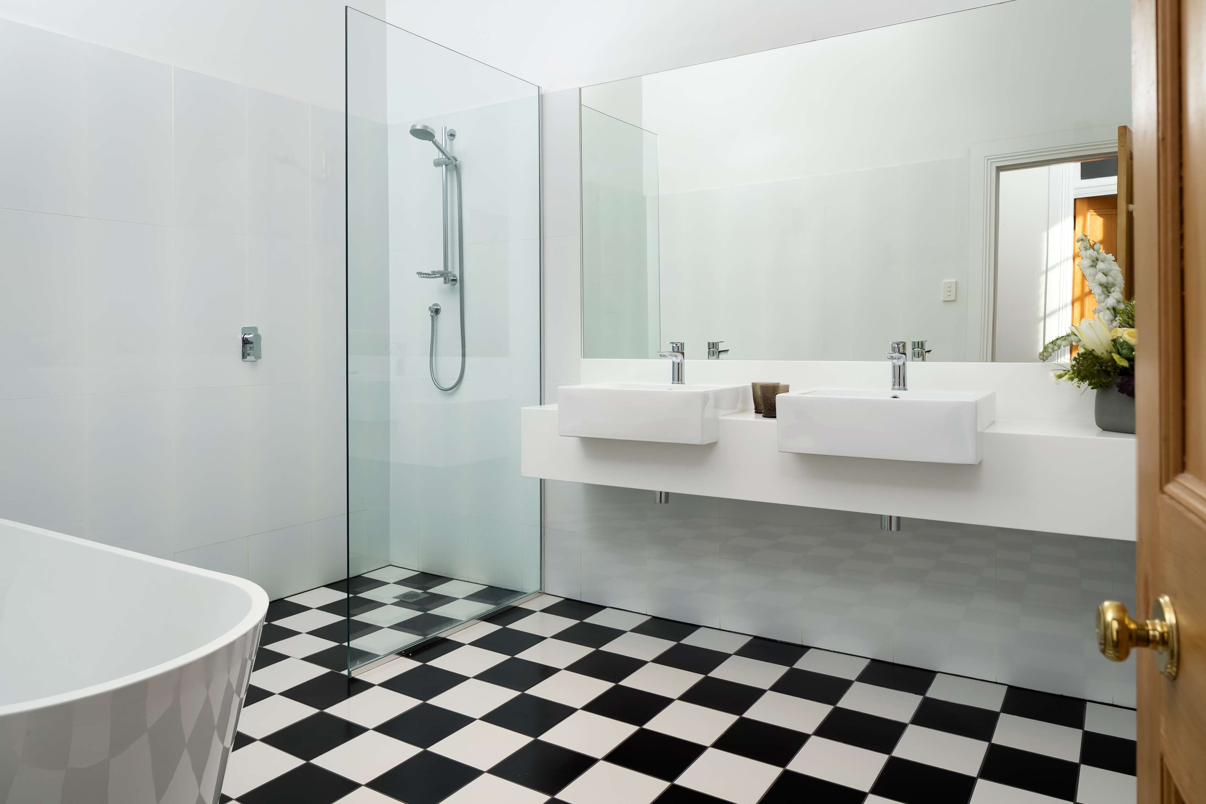 A modern bathroom with a glass shower enclosure, a white sink, and a checkered floor.