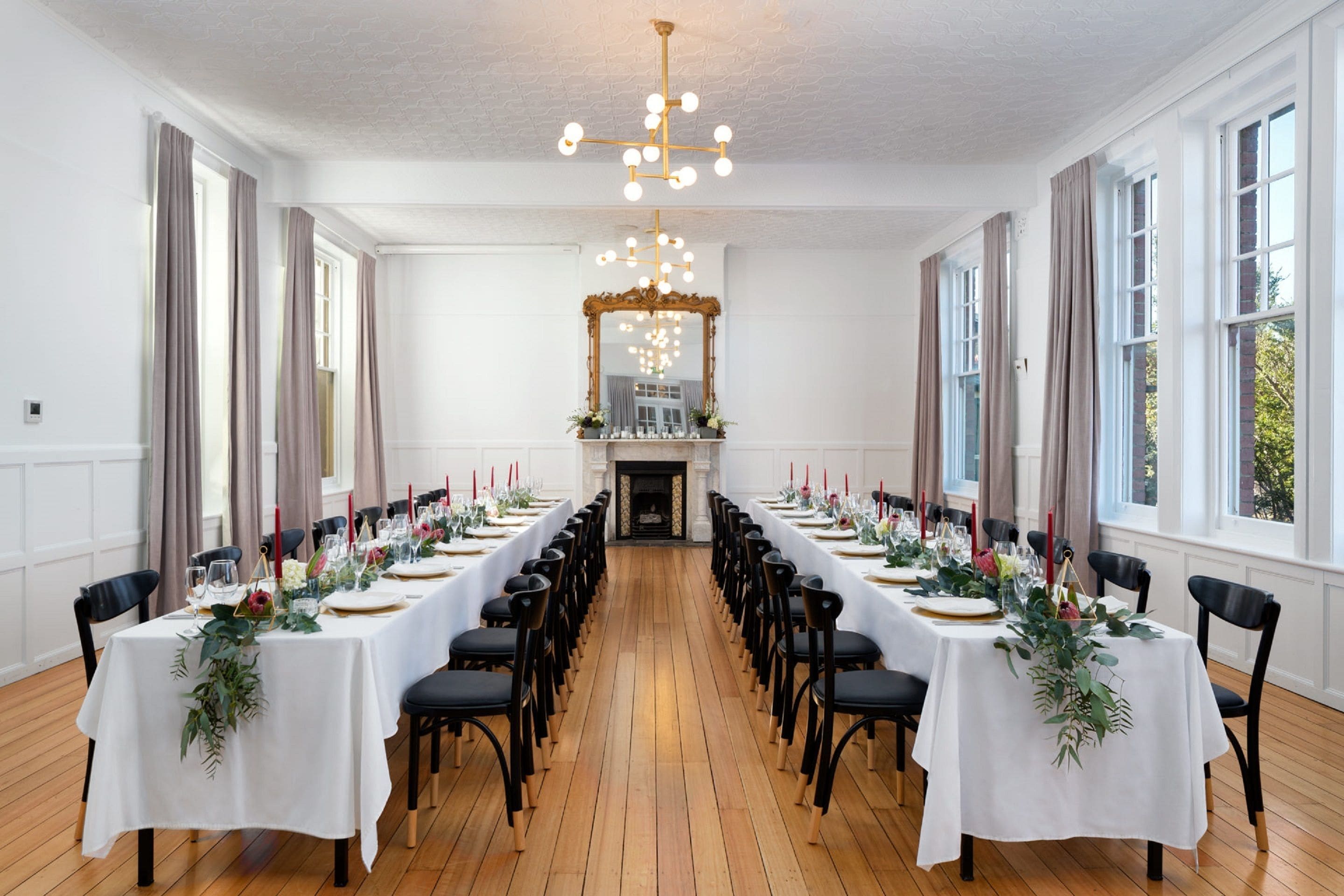 A long dining room with white tablecloths, black chairs, and a chandelier.