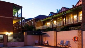 Una piscina con tumbonas y un flotador salvavidas, rodeada de edificios de varios pisos con balcones e iluminación exterior.