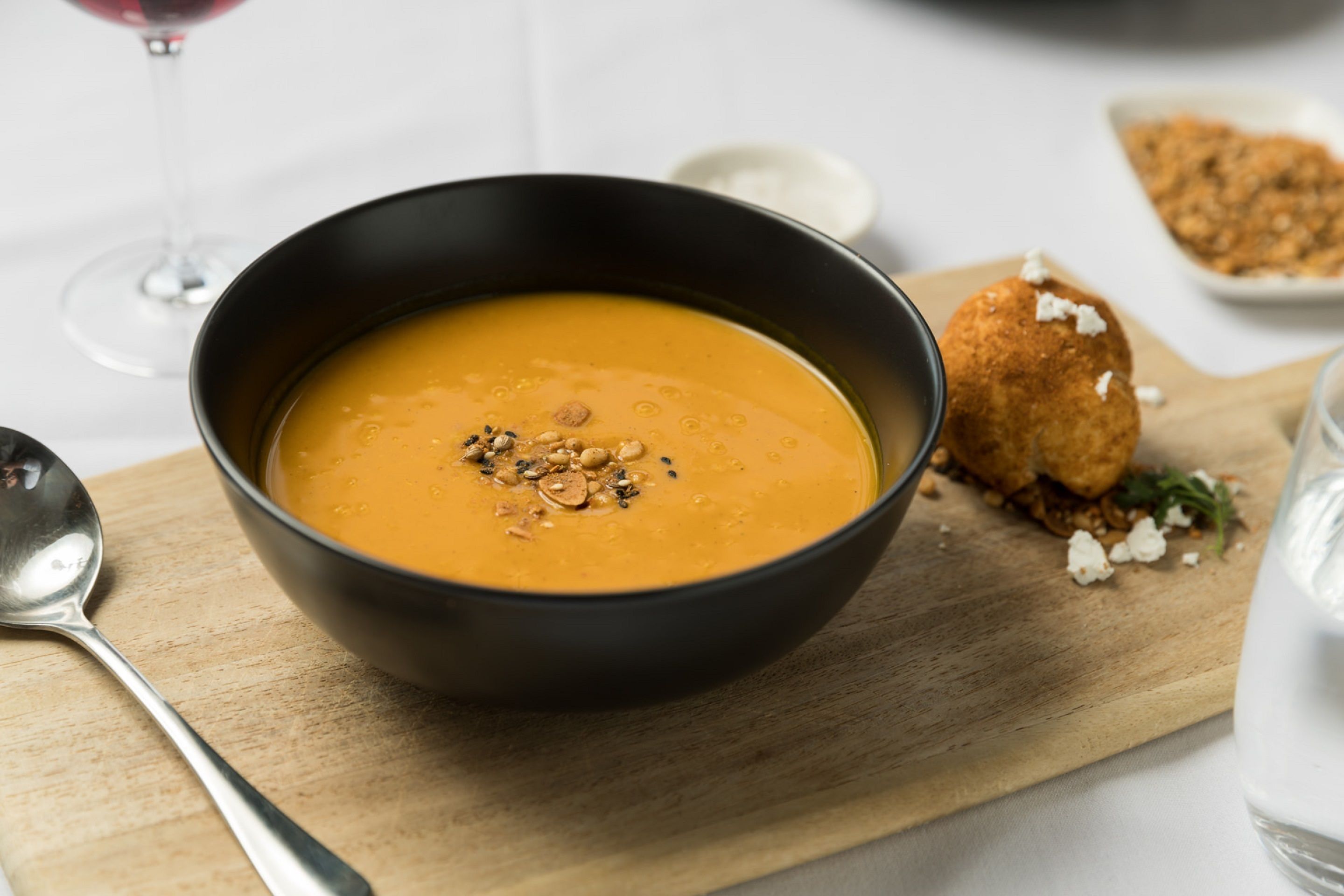 A bowl of soup on a wooden board with a spoon beside it.