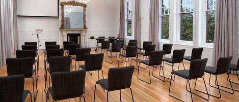 A conference room with a large screen, multiple chairs, a fireplace, and large windows.