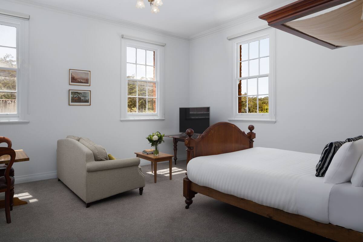 A bedroom with a bed, a sofa, a small table with a vase, and a TV.