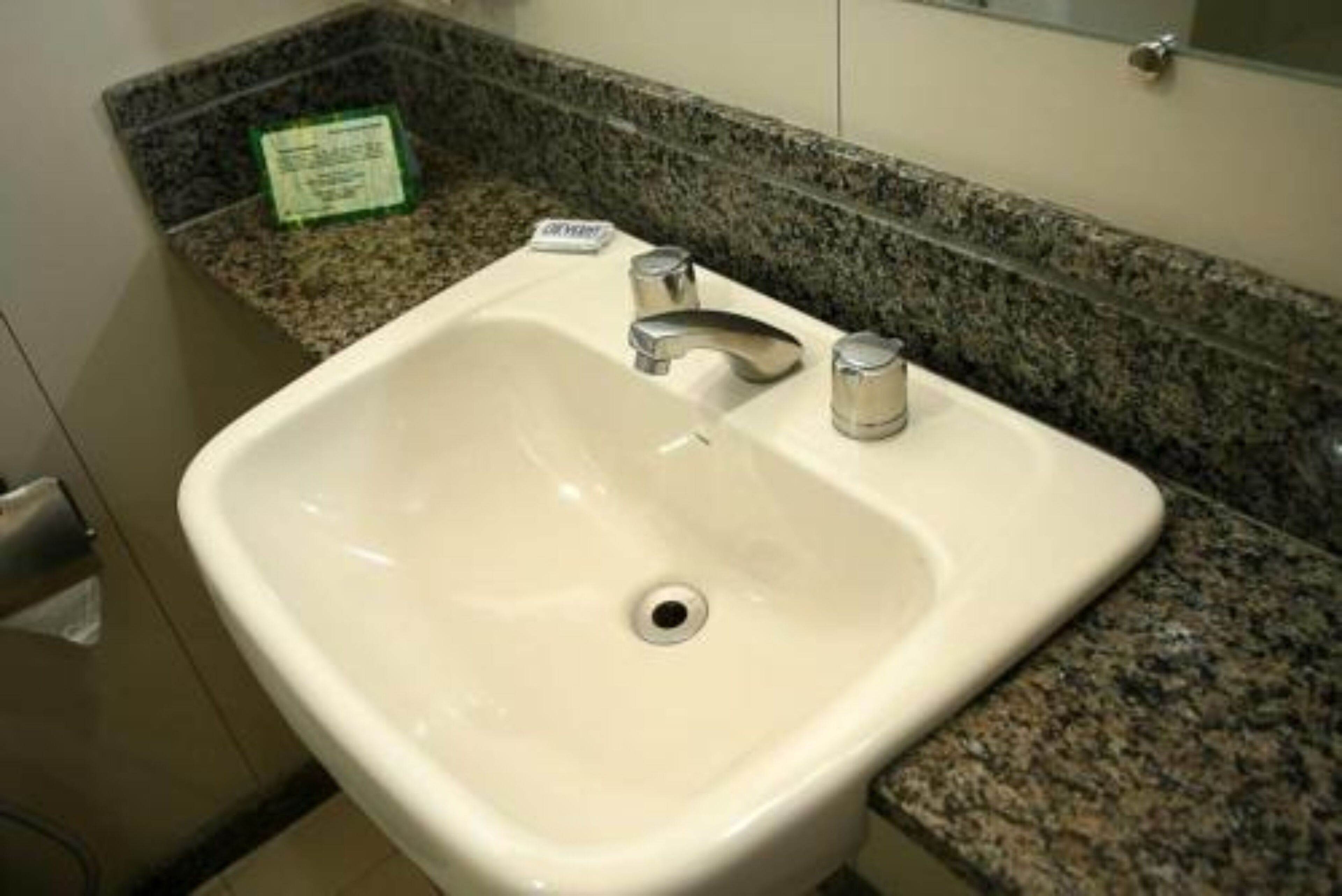 A bathroom sink with a granite countertop, a mirror above it, and a soap dispenser on the counter.