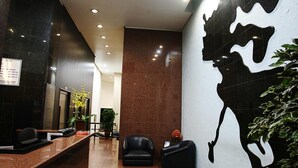 A reception area with a reception desk, a black leather sofa, a potted plant, and a wall with a large black and white mural. - Cheverny Apart Hotel (Belo Horizonte)