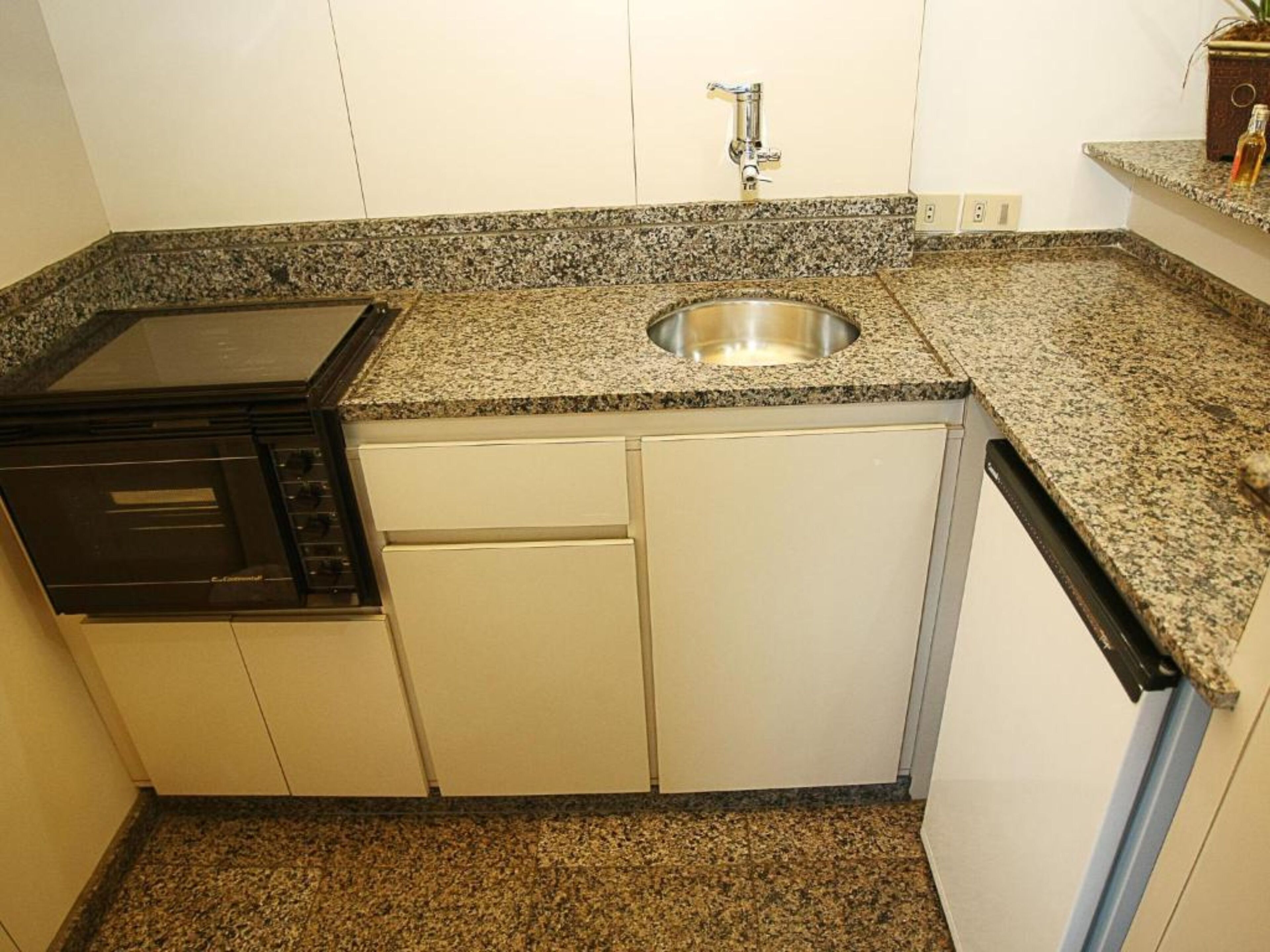 A compact kitchen with a built-in stove, a stainless steel sink, and white cabinetry.
