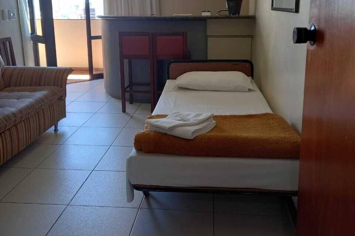 Une chambre d’hôtel avec un lit, une chaise, une petite table, une plante en pot et une vue sur l’extérieur.