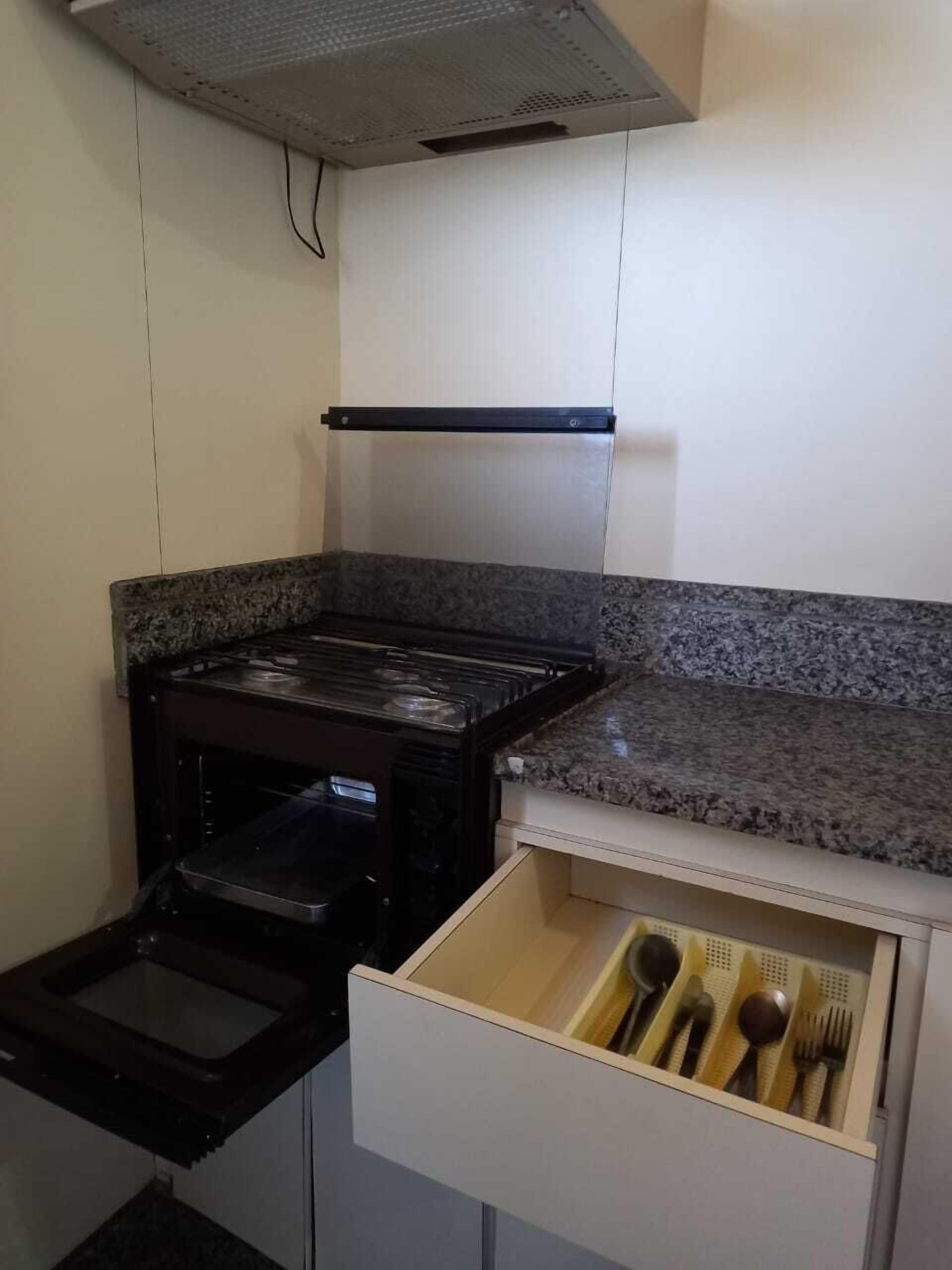 A compact kitchen with a built-in oven, a microwave, and a drawer with utensils.