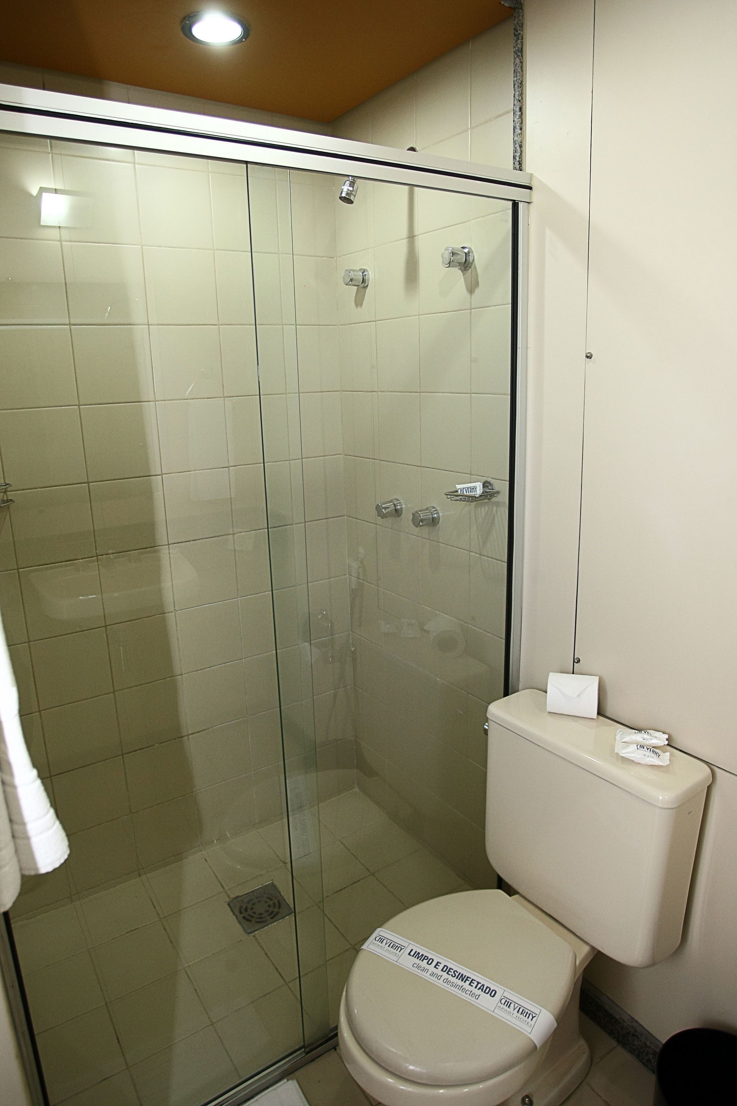 A bathroom with a glass-enclosed shower, a toilet with a lid, and a towel hanging on the wall.