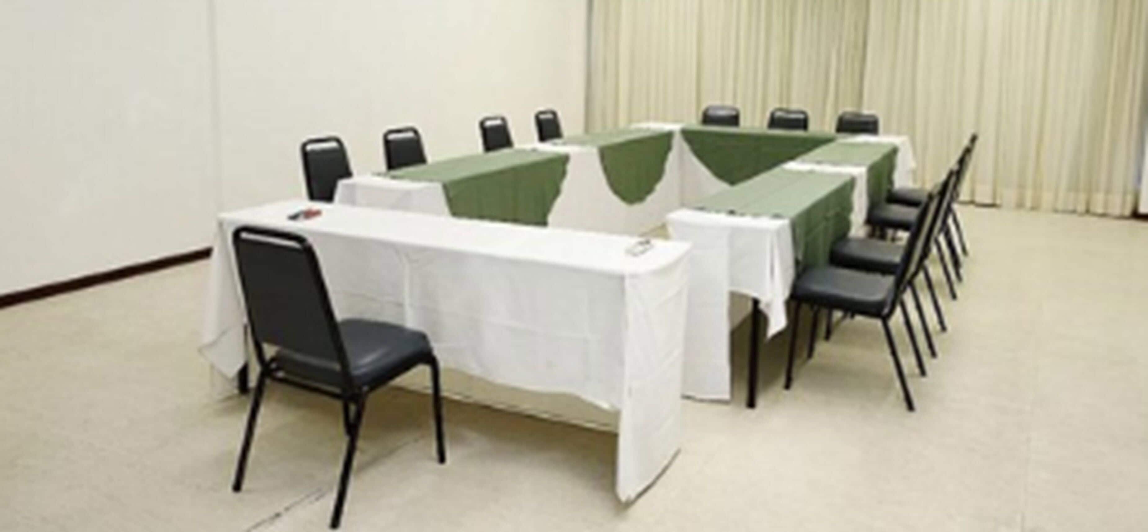 A conference room with a long table and chairs, white tablecloths, and a green runner.