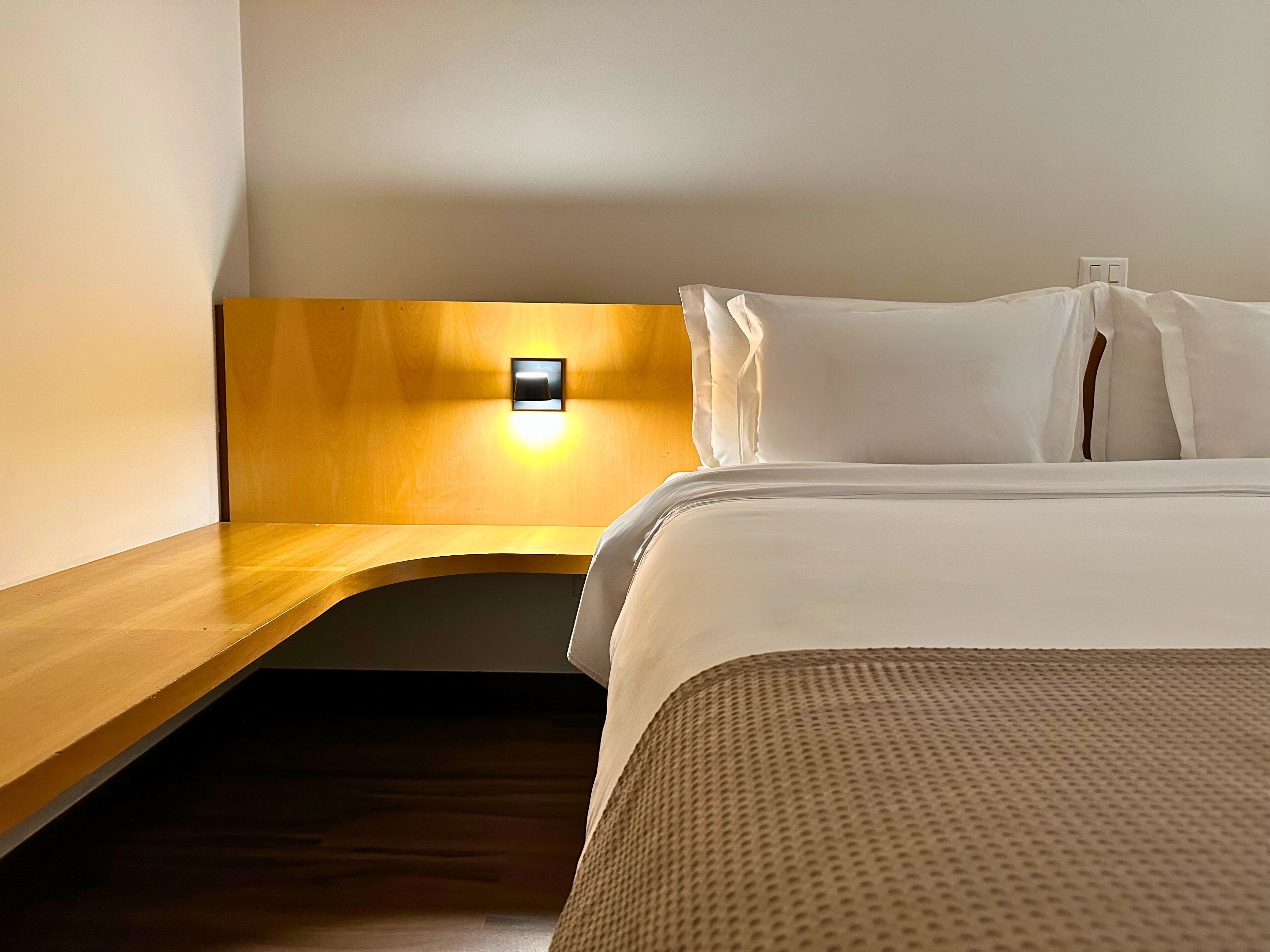 Una habitación de hotel con cabecera de madera, una mesita de noche y una cama con ropa blanca.