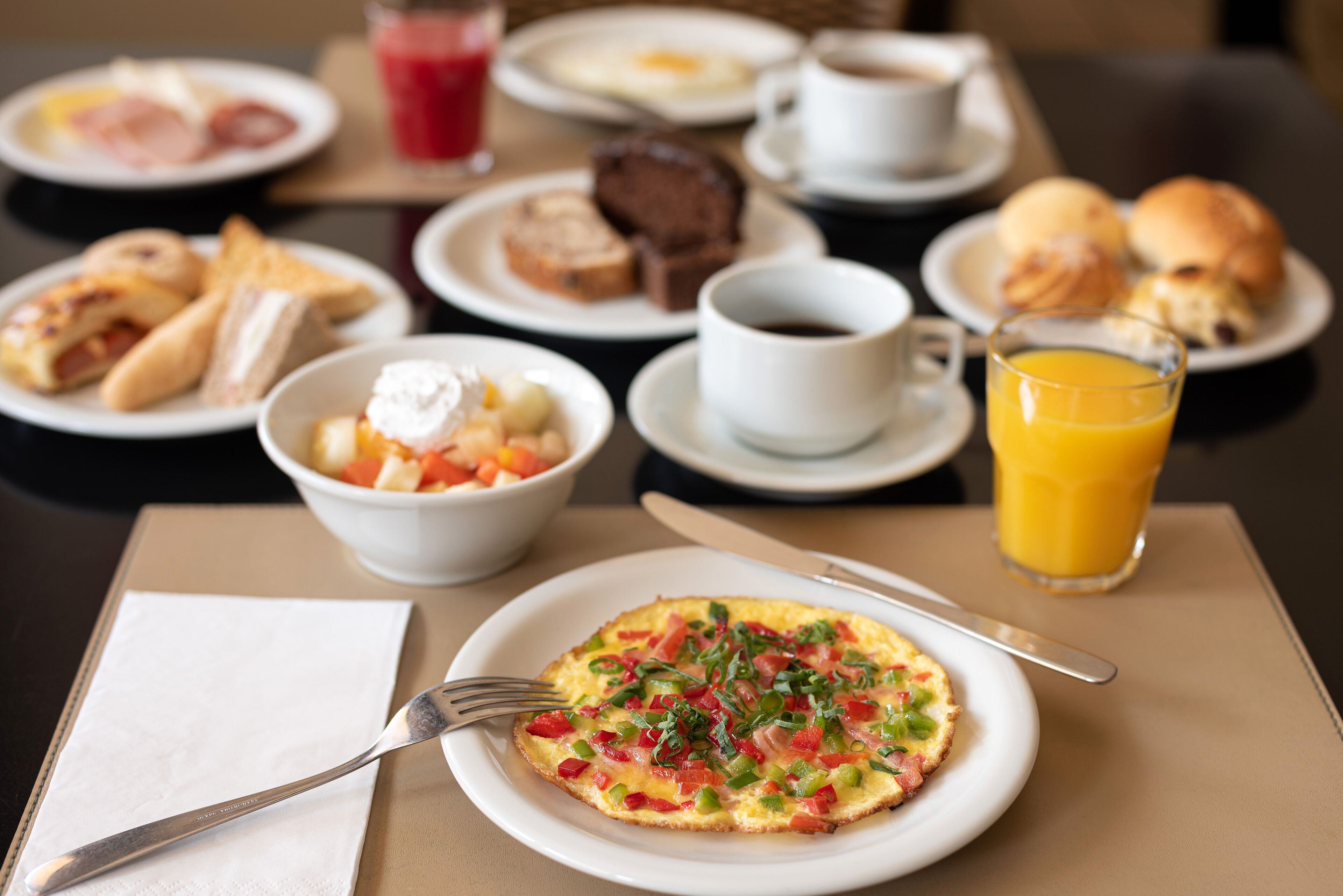 Une table dressée pour le petit-déjeuner, avec différents plats, notamment une omelette, des toasts et un bol de fruits.