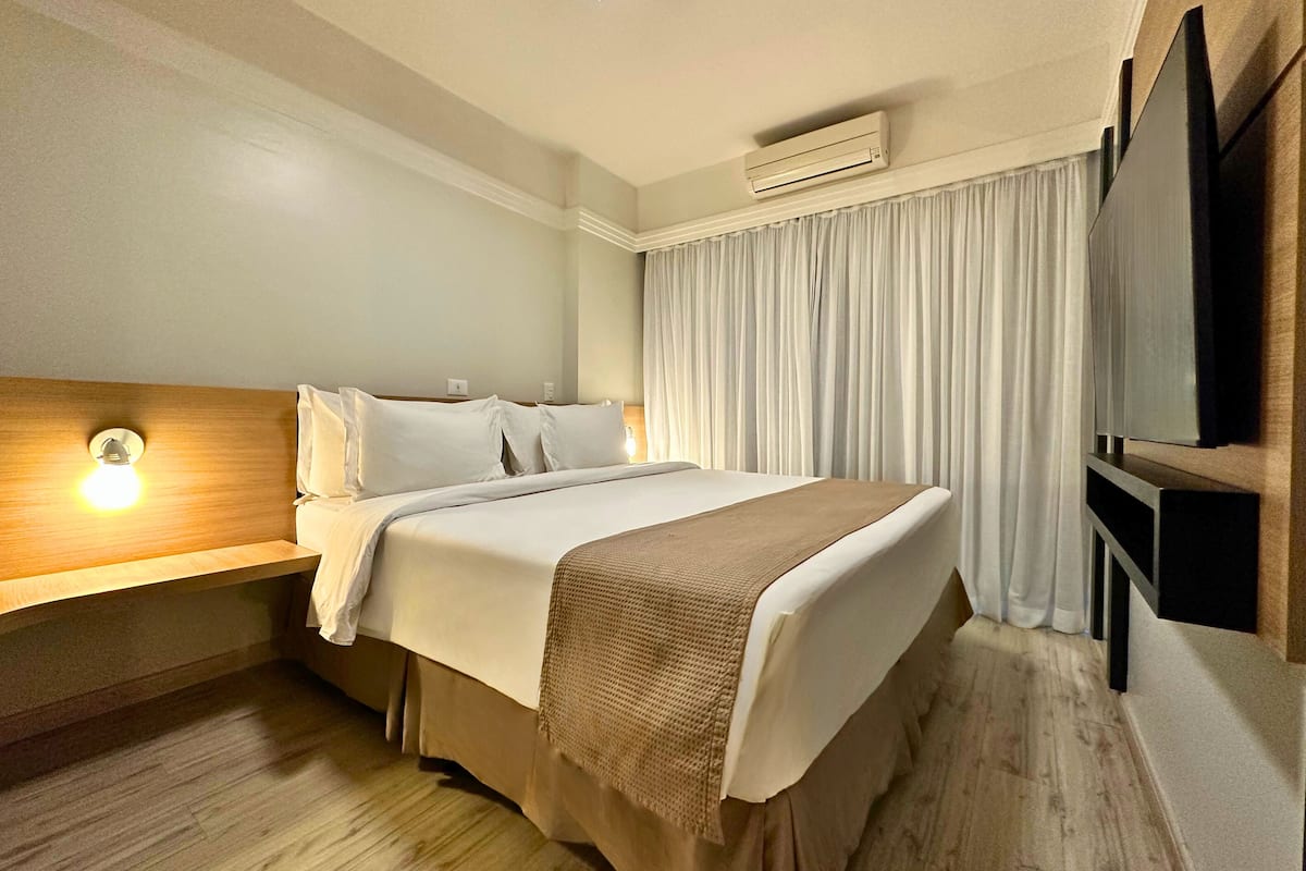 Une chambre d’hôtel équipée d’un lit, d’une table de chevet avec une lampe, d’un téléviseur à écran plat et d’un appareil de climatisation.