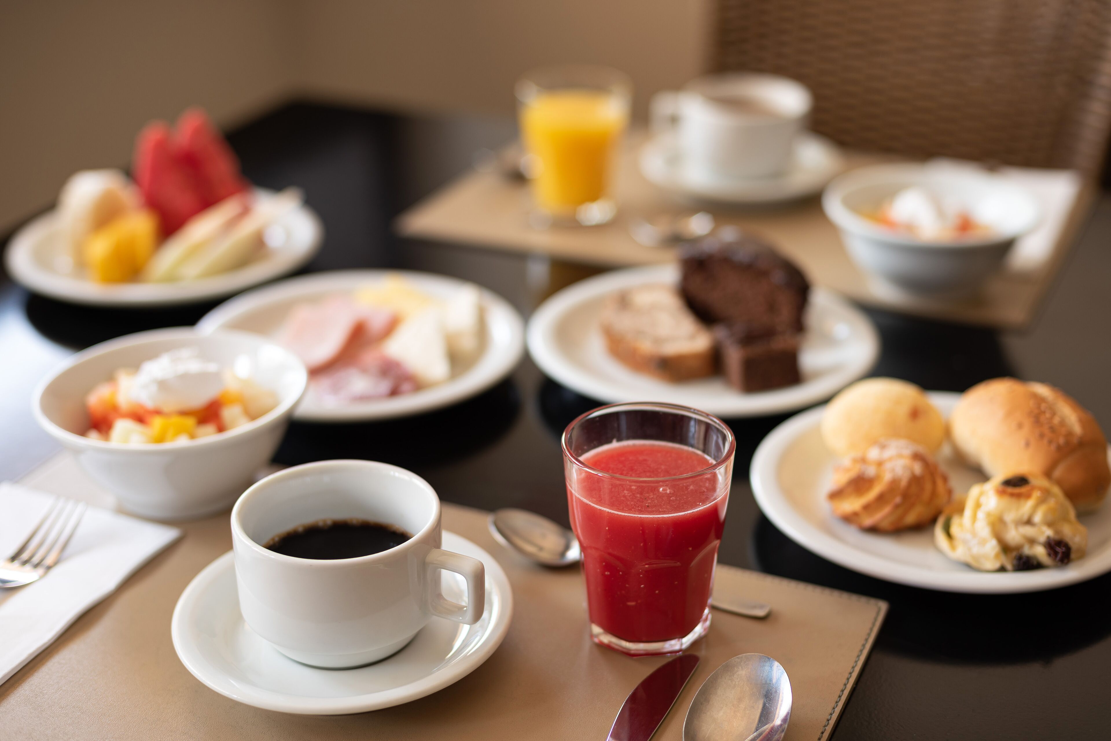 A breakfast table with plates of food, a cup of coffee, a glass of juice, and a bowl of soup.
