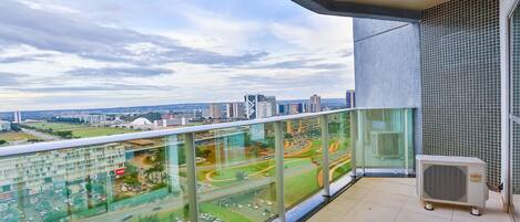 A balcony with a glass railing overlooking a cityscape with buildings and roads.