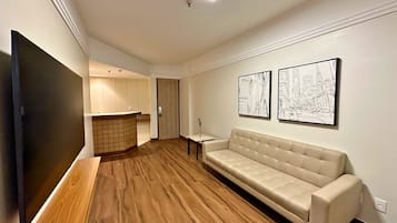 Uma sala de estar moderna com uma televisão de tela plana grande, um sofá bege, piso de madeira e duas obras de arte com tema urbano.
