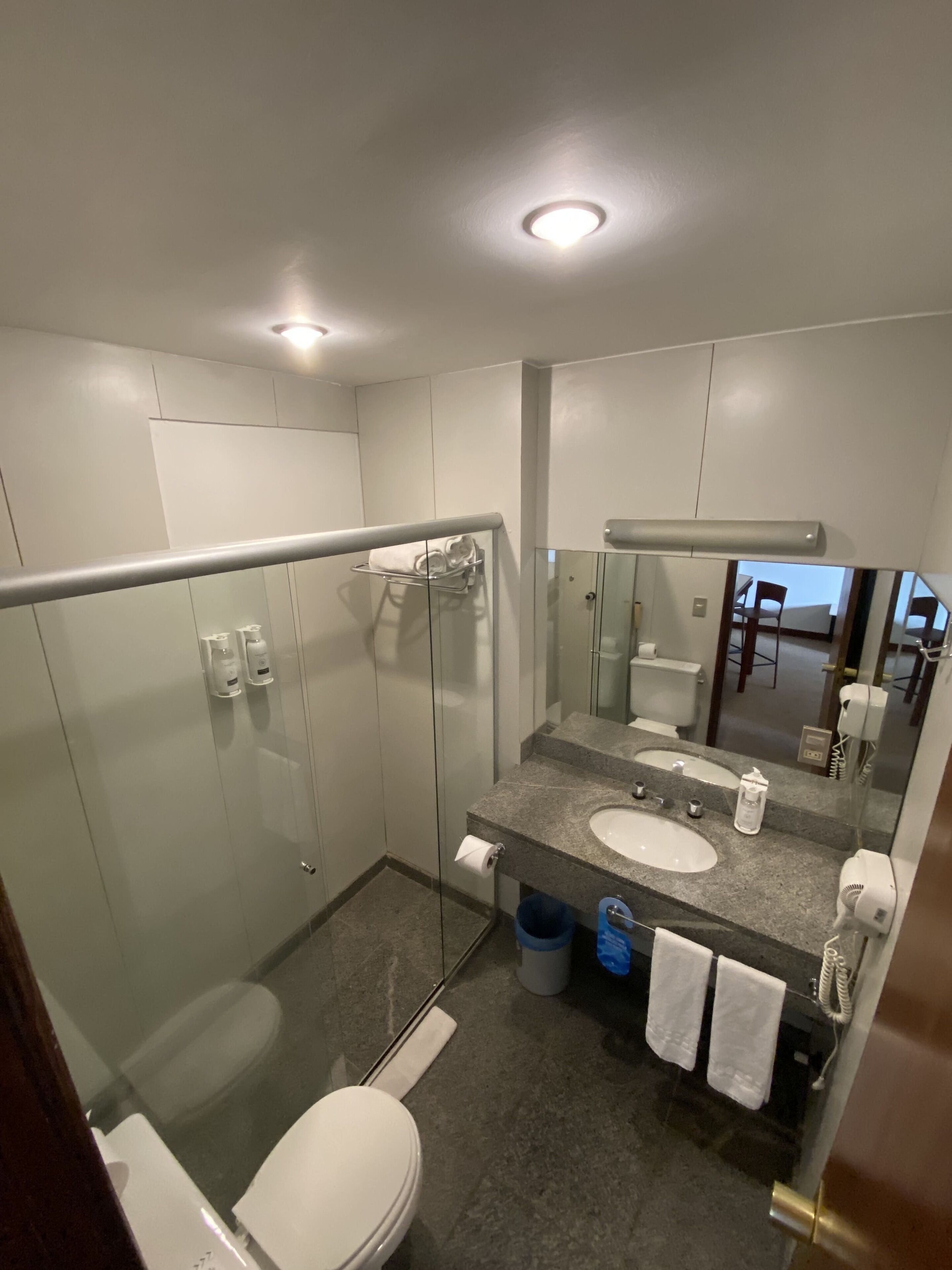 Une salle de bain moderne avec une douche à parois de verre, des toilettes blanches, un lavabo en granit avec un miroir et un porte-serviettes.