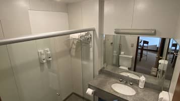 Un baño moderno con cabina de ducha de vidrio, un inodoro blanco, un lavabo de granito con espejo y un perchero para toallas.
