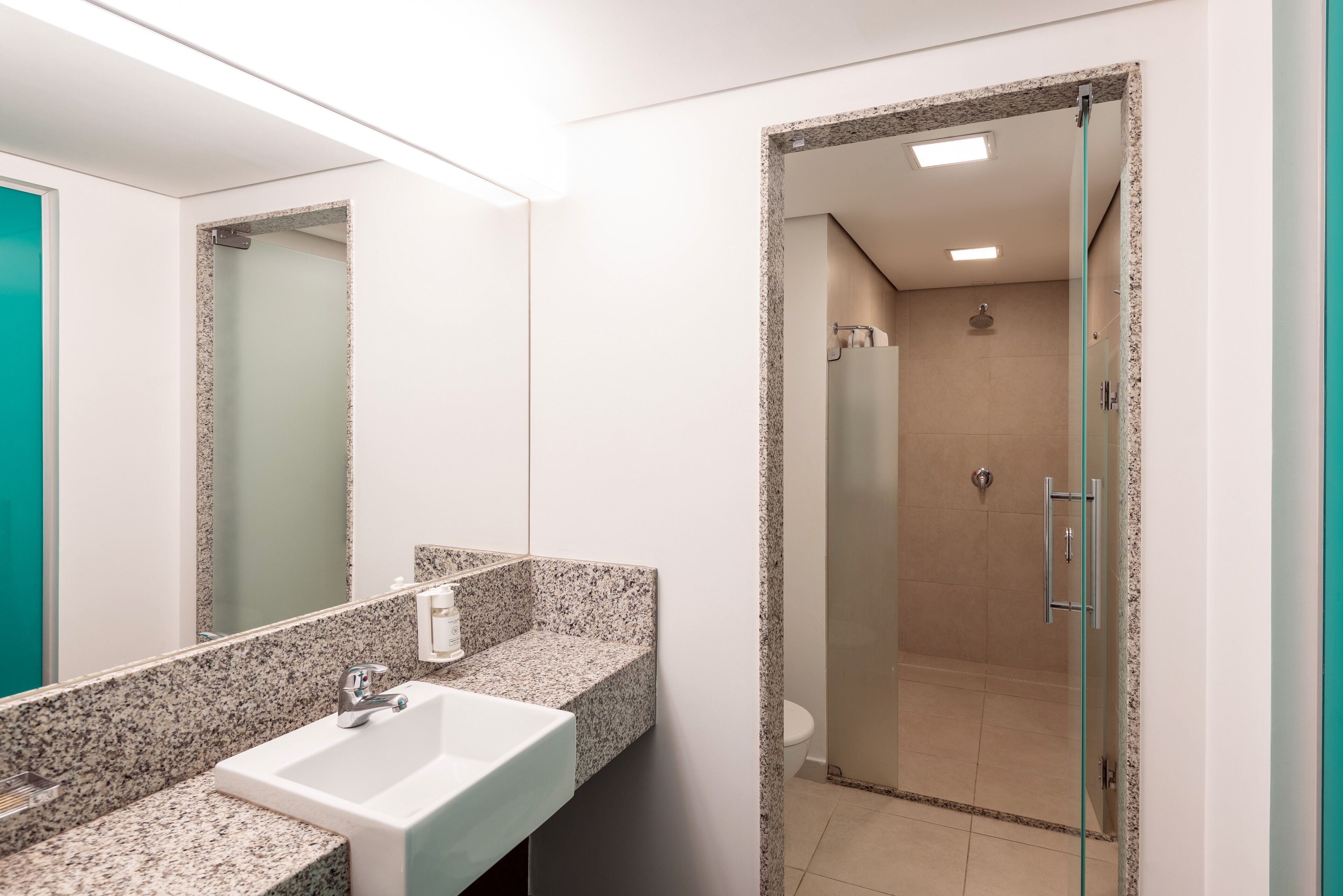 Un baño moderno con lavamanos de granito, un espejo grande y zona de ducha con mampara de vidrio.