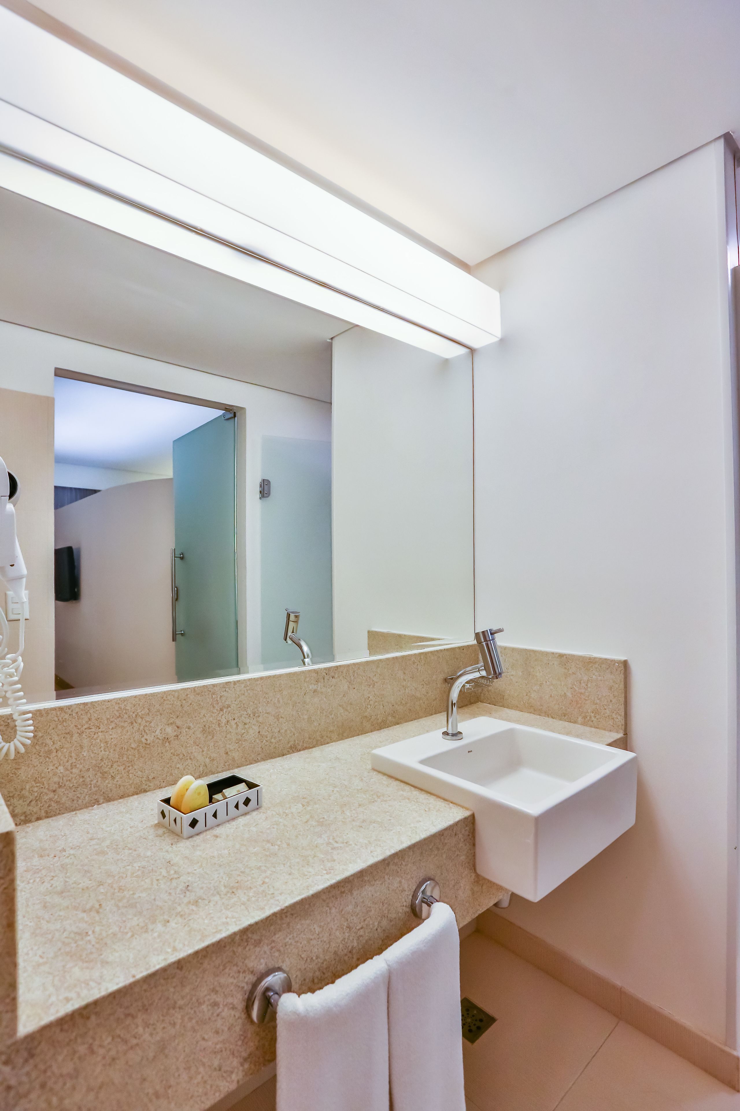 A modern bathroom with a large mirror, a sink, and a countertop with a fruit basket.