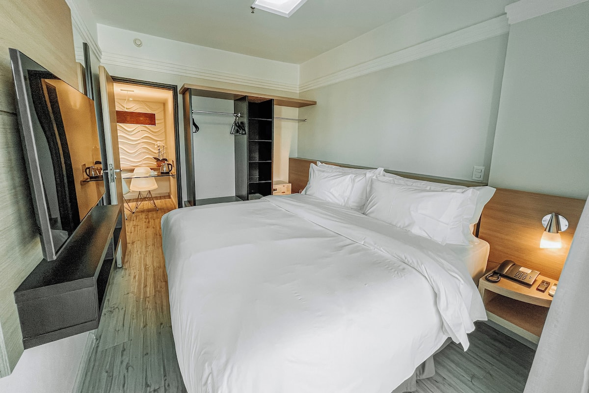 Une chambre d’hôtel avec un grand lit, une table de chevet avec une lampe, une armoire et un miroir.