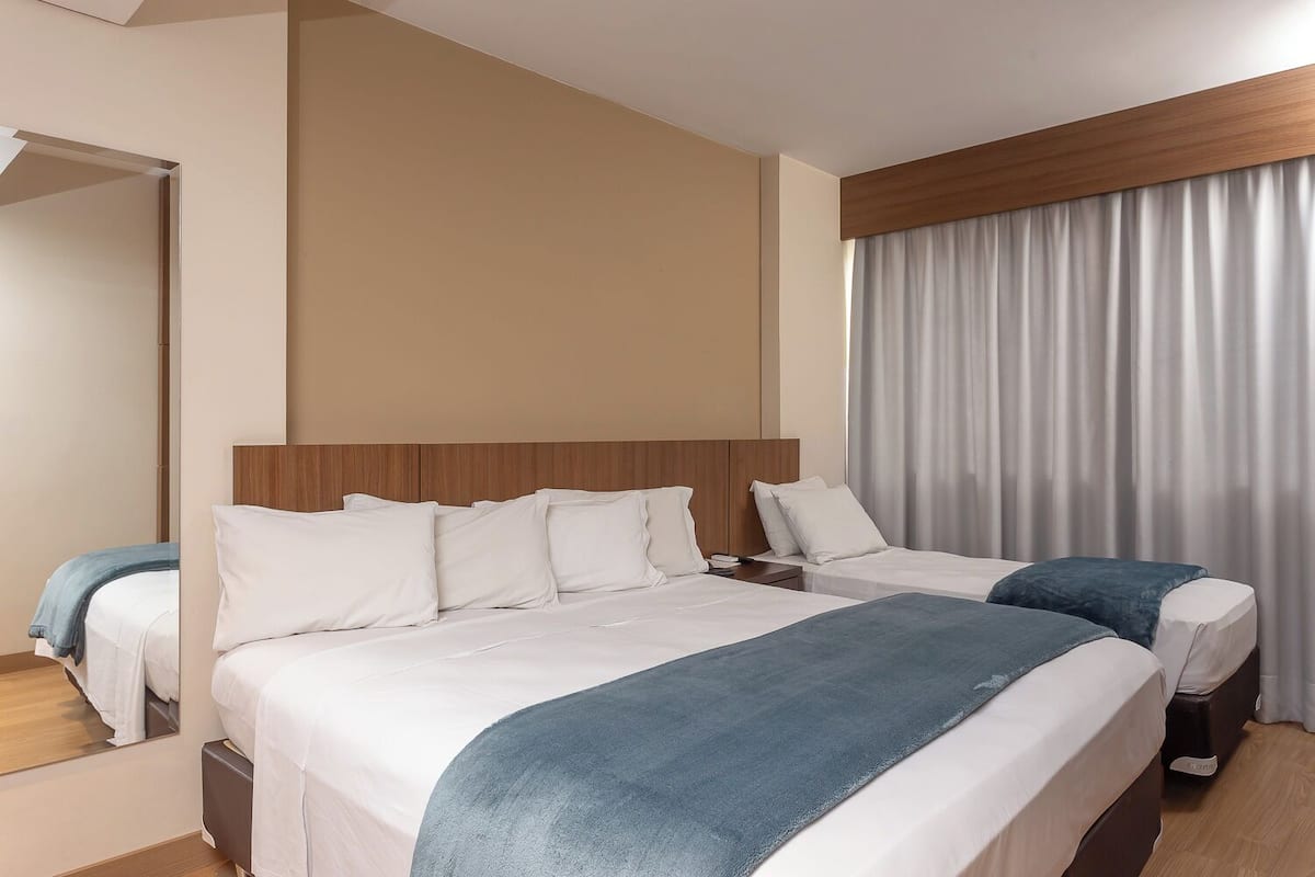 A hotel room with two beds, a wooden headboard, a large mirror, and a view of a curtain-covered window.