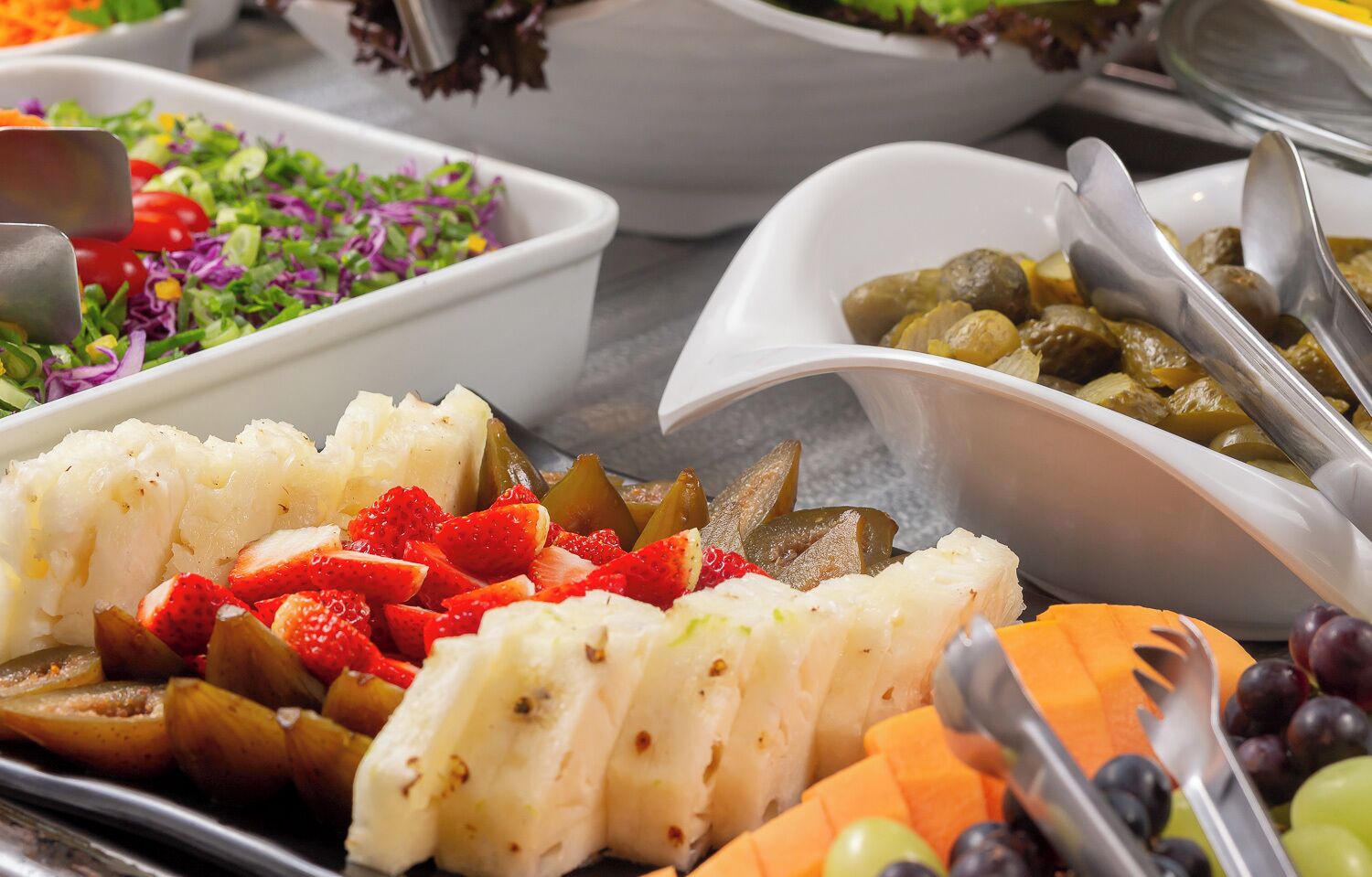 A buffet with various food items including fruits, vegetables, and a salad.