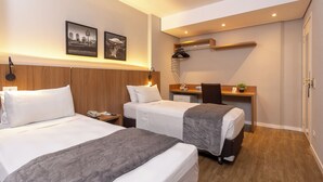 A hotel room with two beds, a desk, a chair, a small table, a potted plant, and a wall-mounted shelf. - Roochelle Hotel by Nobile (Curitiba)