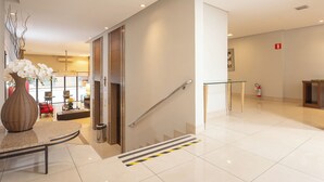 A modern hotel lobby with a reception desk, a staircase with a handrail, and a fire extinguisher on the wall. - Roochelle Hotel by Nobile (Curitiba)