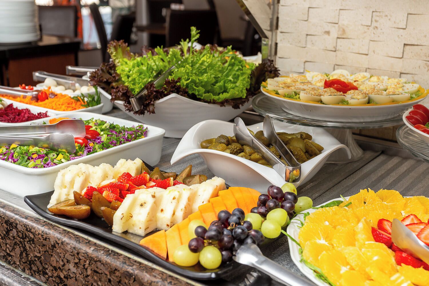 A buffet with various dishes including fruits, vegetables, and salads.