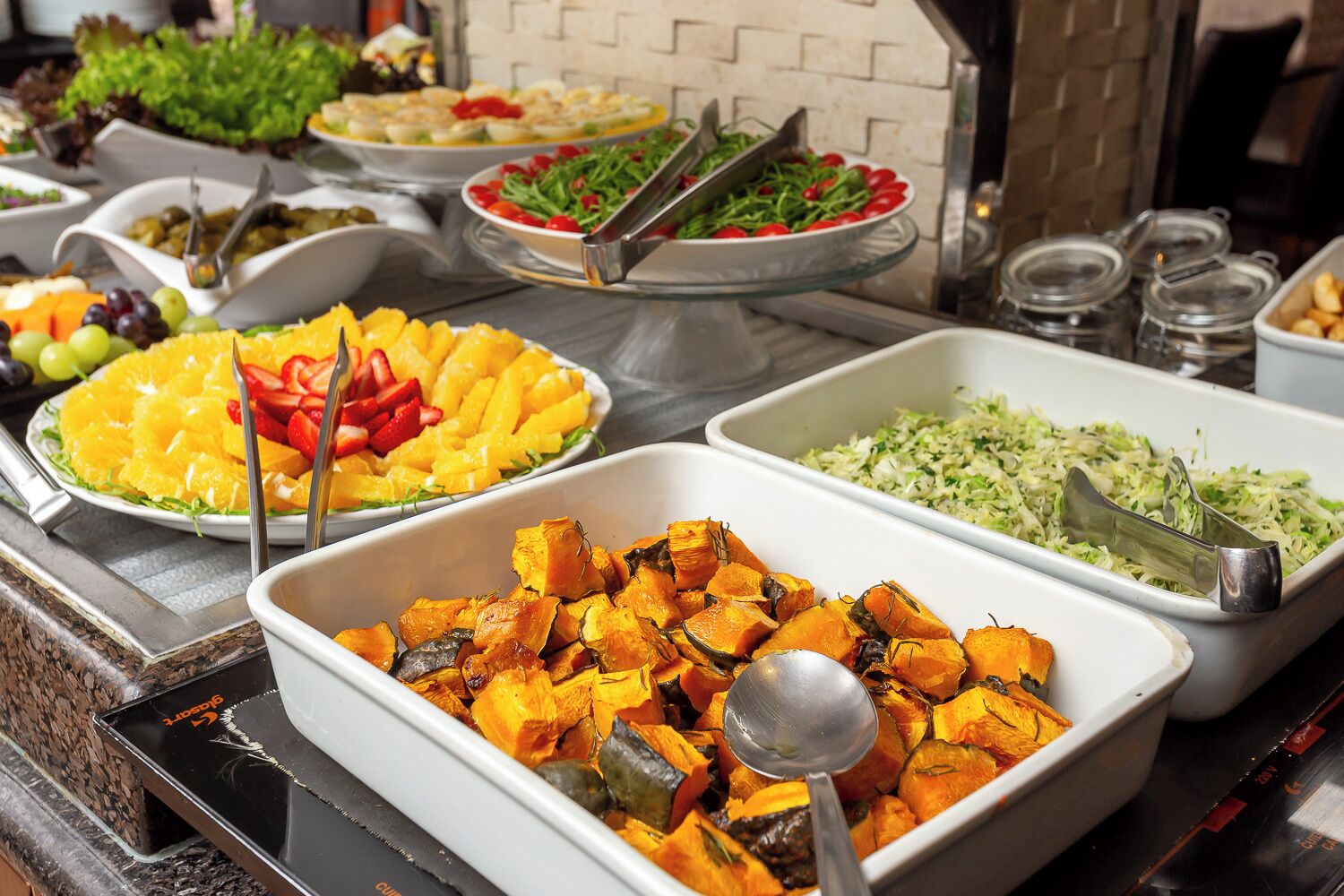 A buffet with various dishes including fruits, vegetables, and salads.