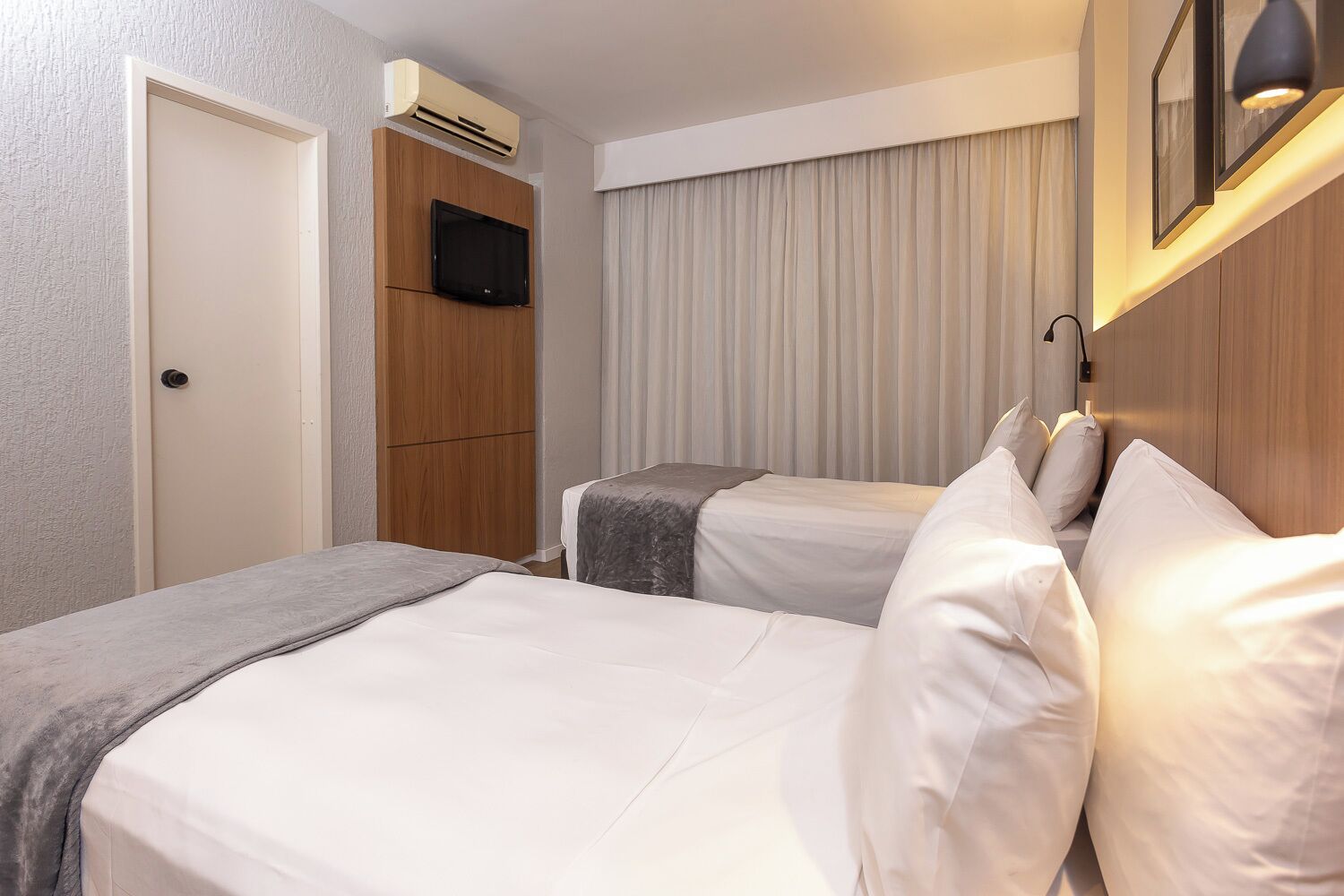 Habitación de hotel con dos camas, televisión, aire acondicionado y una ventana con cortinas.