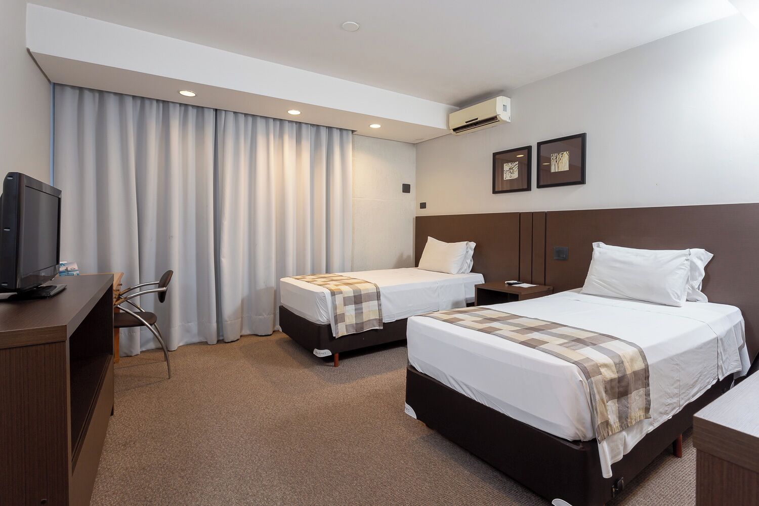 Een hotelkamer met twee bedden, een bureau met een computer, een stoel en een airconditioning.