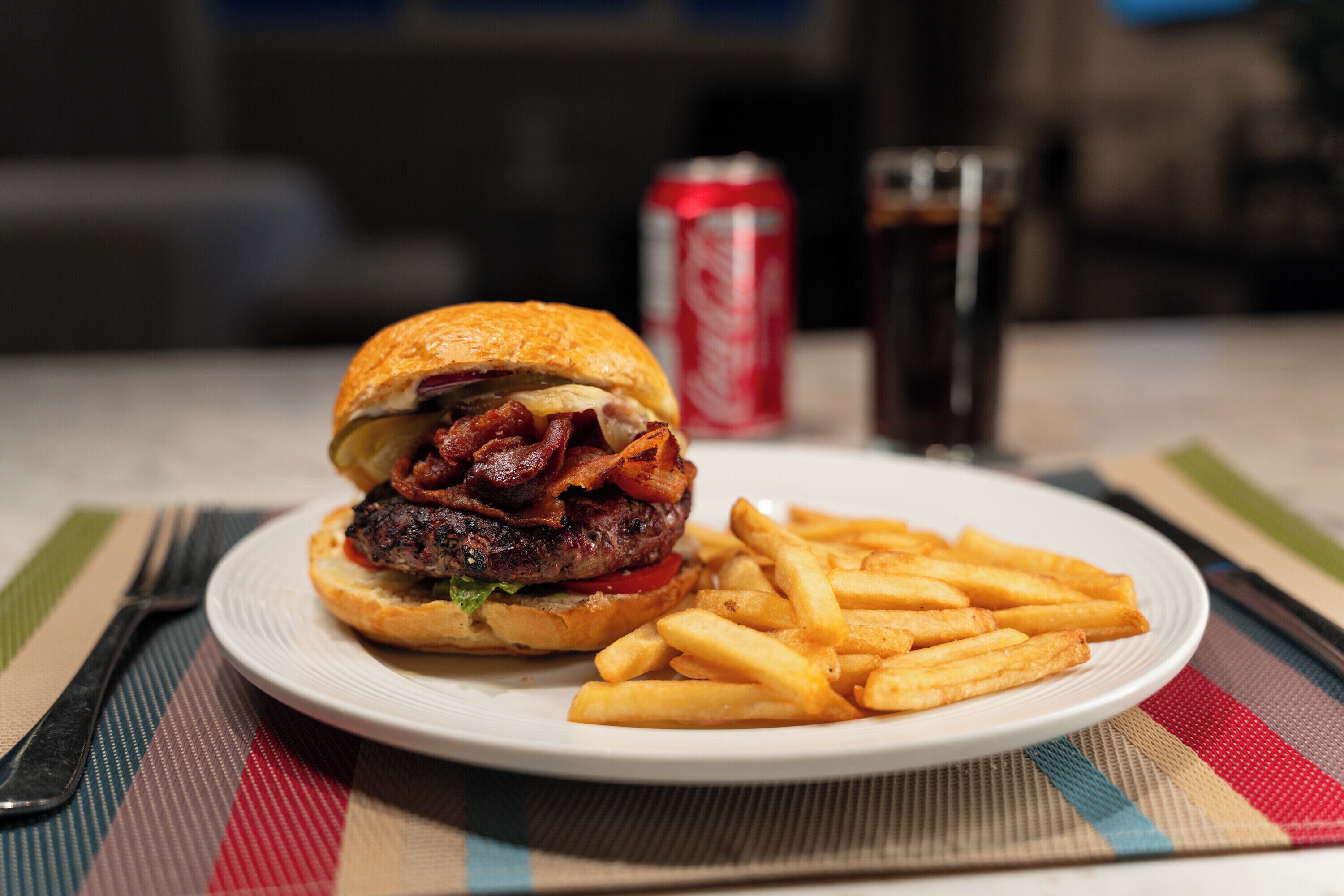 Une assiette avec un hamburger et des frites, une canette de soda et des verres sur une table.