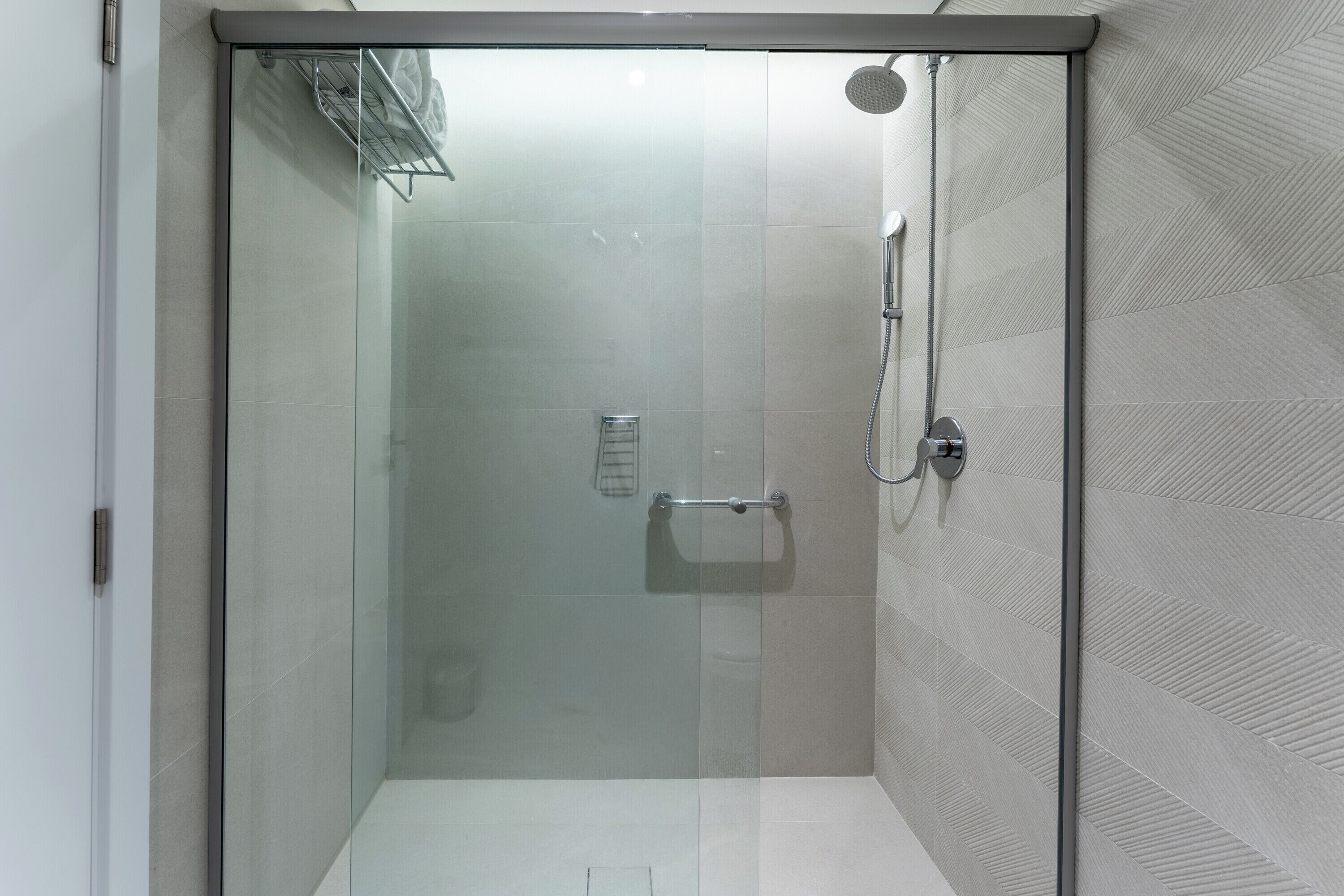 A modern shower stall with a glass door, a handheld showerhead, and a towel rack.