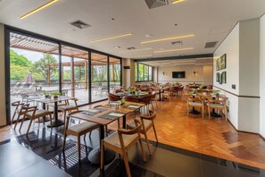 A spacious indoor dining area with multiple tables and chairs, large windows offering a view of the outdoors, and a flat-screen TV mounted on the wall. - Deville Prime Maringá (Maringá)