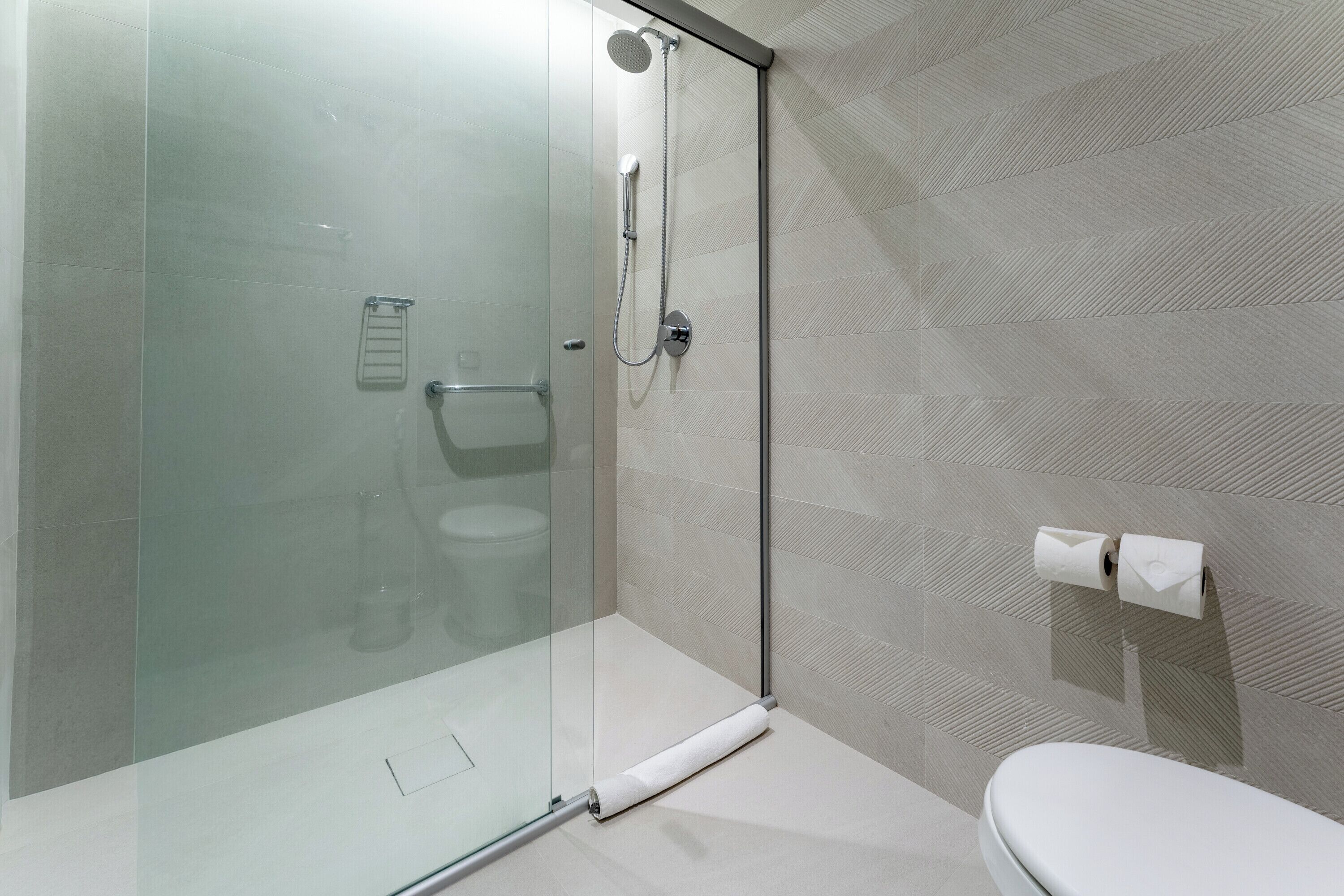 Un baño moderno con ducha envuelta en vidrio, inodoro y dispensador de toallas.