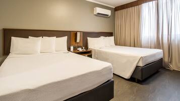 Een hotelkamer met twee bedden, een nachtkastje, een airconditioner en een raam met gordijnen.