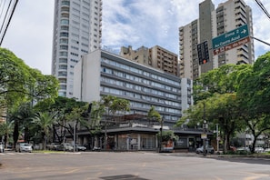 Un hôtel à plusieurs étages, doté d’une façade moderne, situé à un carrefour où l’on peut voir des feux de signalisation et des panneaux indicateurs.