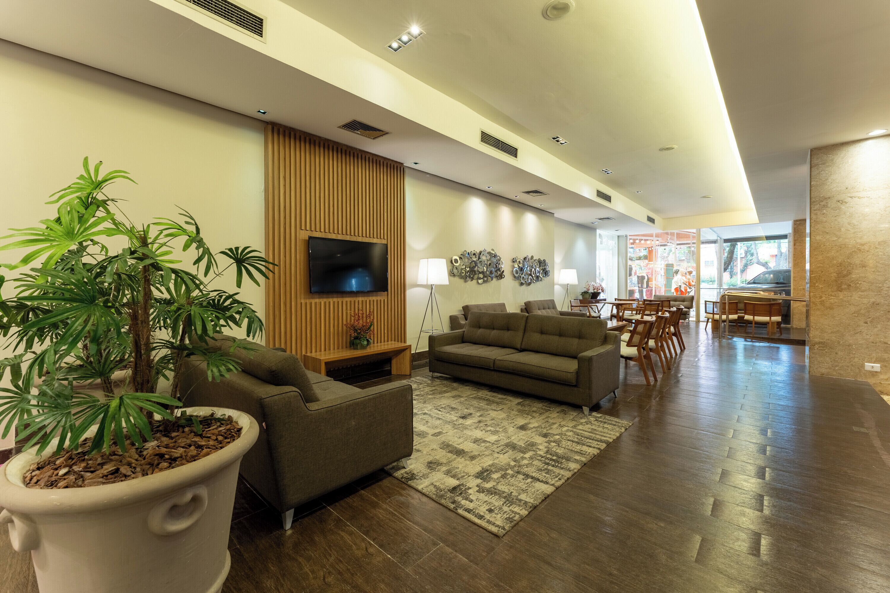 A modern living room with a flat-screen TV, sofas, a coffee table, and a large potted plant.