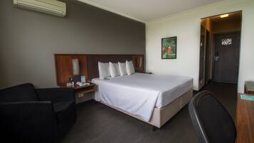 Ein Hotelzimmer mit einem Bett, einem Schreibtisch, einem Stuhl, einem Nachttisch und einer Wand-Klimaanlage.