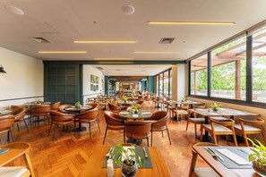 A spacious restaurant with multiple dining areas, wooden furniture, and large windows offering views of the outdoors. - Deville Prime Maringá (Maringá)