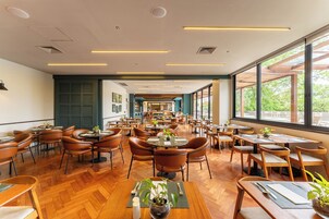 Un restaurante espacioso con varias zonas de comedor, mobiliario de madera y amplios ventanales que ofrecen vistas al exterior.