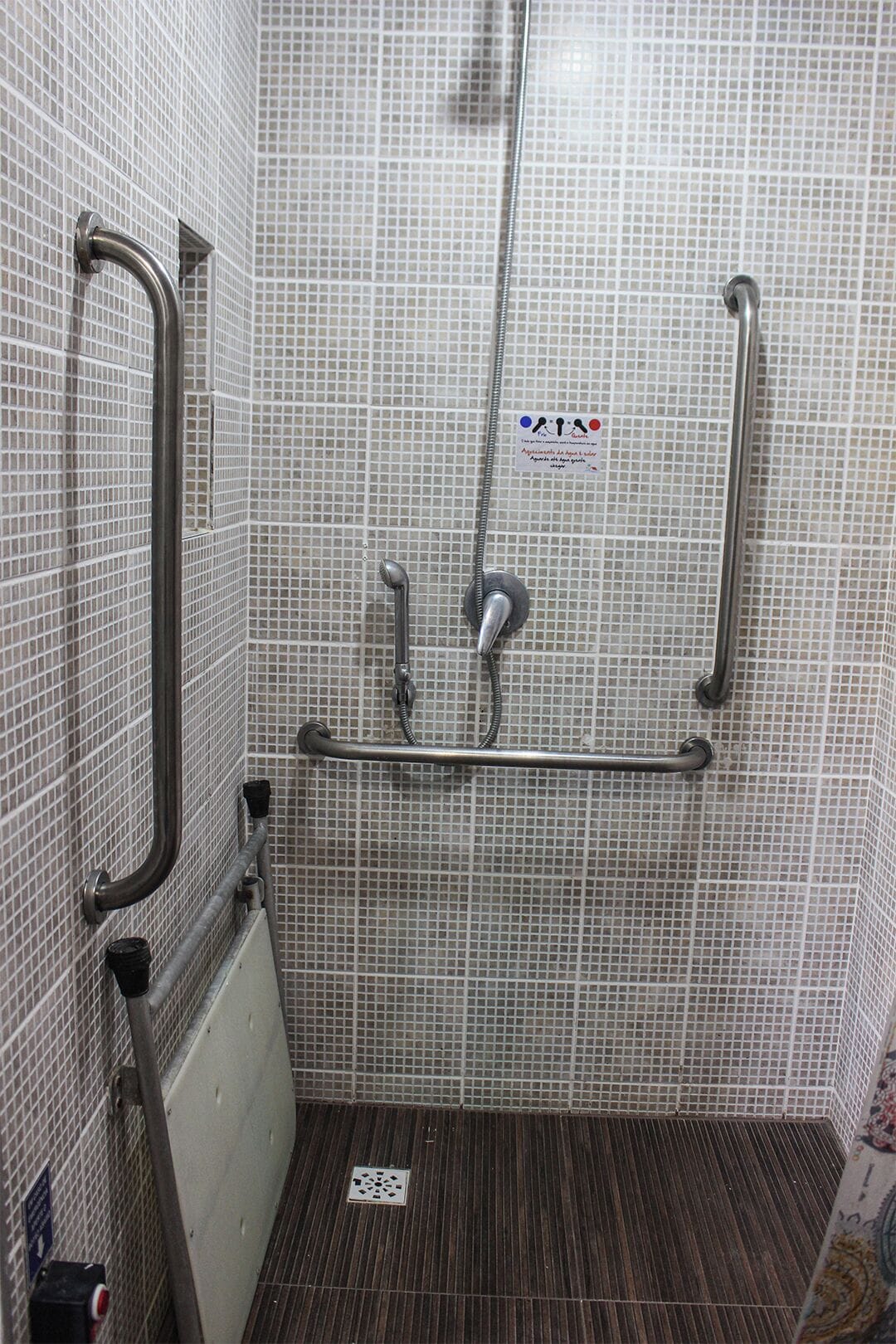Zona de ducha con pared de azulejos, barandilla, ducha y panel de control.