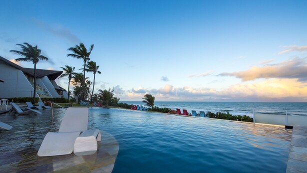 A poolside area with lounge chairs, palm trees, and a view of the ocean at sunset. - GoldMen Vila do Mar Natal (Natal)
