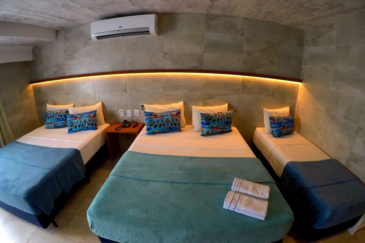 Habitación de hotel con cabecera curvada, dos camas individuales, una cama doble y una mesita de noche con teléfono.