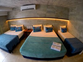 A hotel room with a curved headboard, two single beds, a double bed, and a bedside table with a phone.