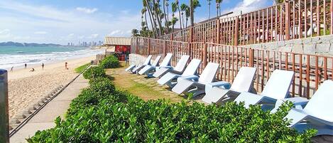 A beachside hotel with rows of sun loungers, palm trees, and a view of the ocean.
