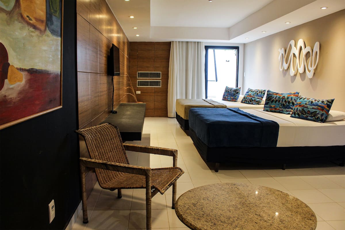 Una habitación de hotel moderna con una cama grande, una zona de estar con una silla, una mesita pequeña y un cuadro en la pared.