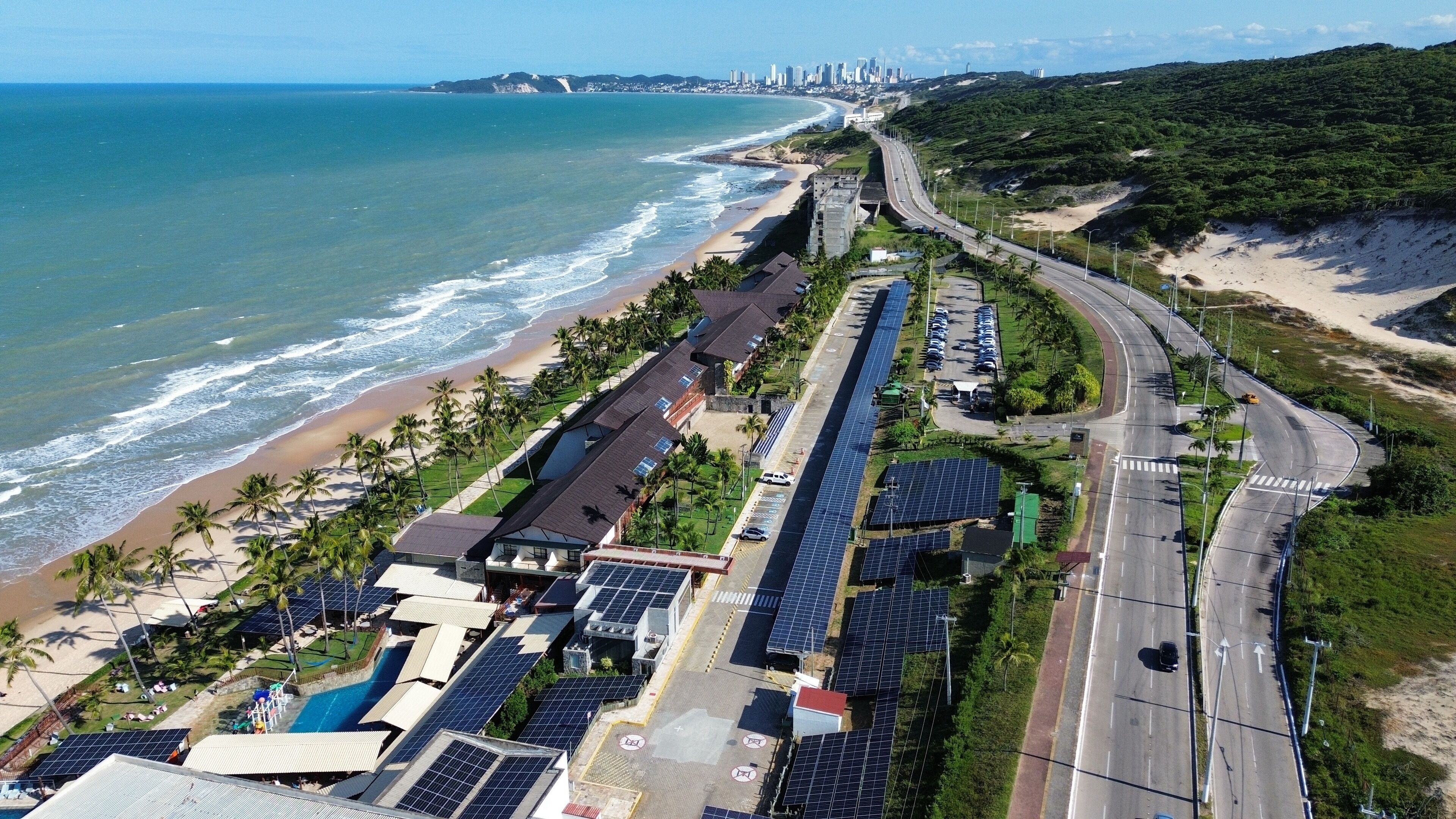 Un hotel frente al mar con vistas a la playa, paneles solares y aparcamiento.