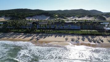 Ein Küstenhotel mit Blick auf den Strand, Palmen und einem Bergpanorama.